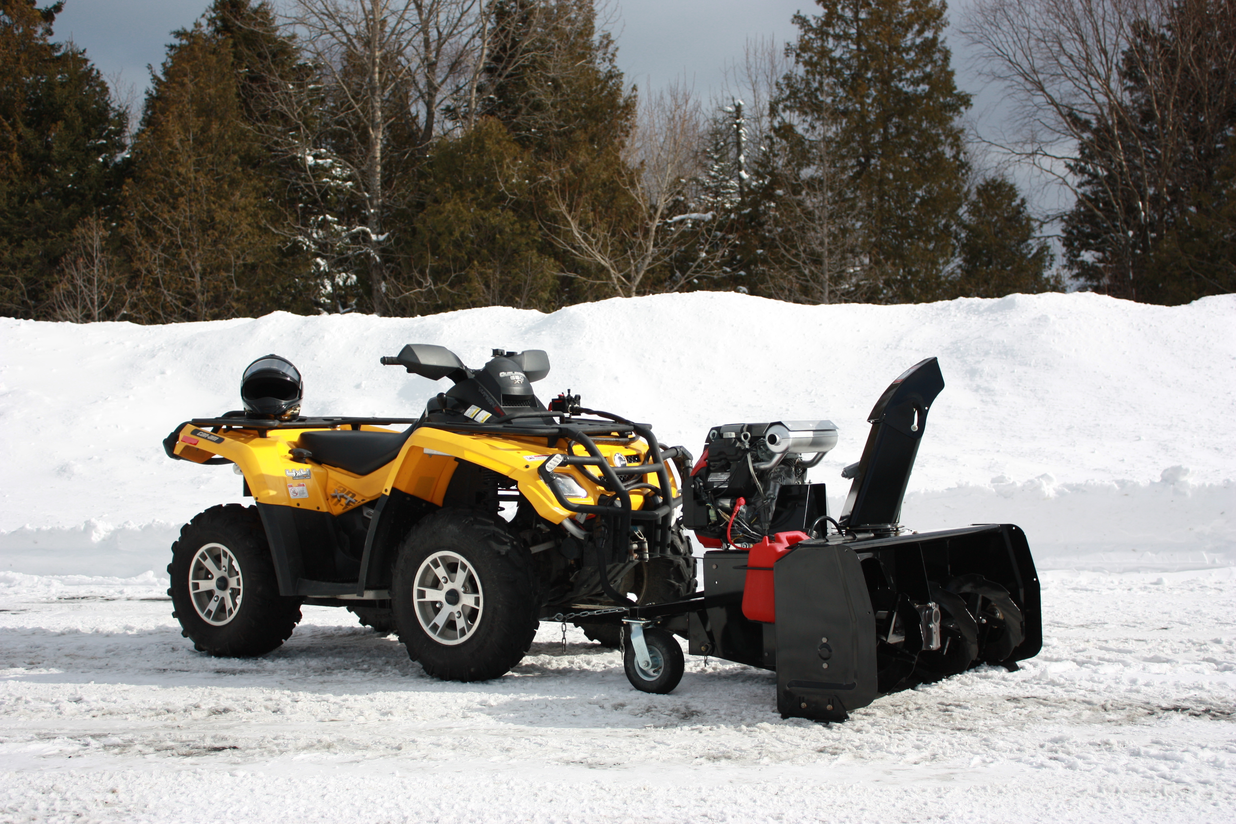 A front-facing image of an Arctic Cat Snowblower by Bercomac, installed on an ATV and parked on snowy terrain.
